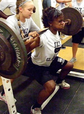 Image: Sophomore state champion sprinter, Kortnei Johnson can leap out of the gym, as well. Here, teammate Jaclynn Lewis spots Johnson during her lift.