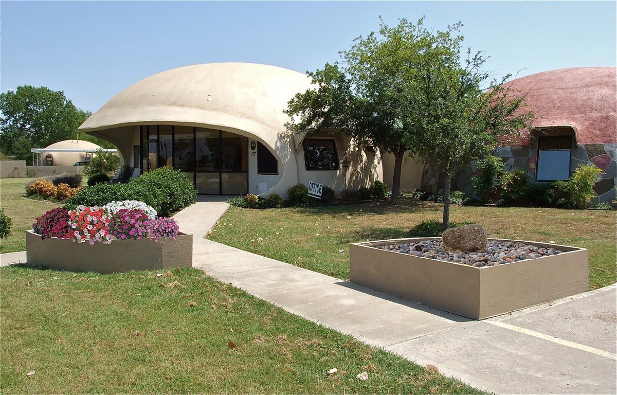 Image: A pair of concrete planters enhance the entrance to the main offices of Monolithic Constructors, Inc. in Italy, Texas. The left planter contains a variety of flowers while the planter on the right is a rock garden featuring one stone which is the meaning of the word monolithic.