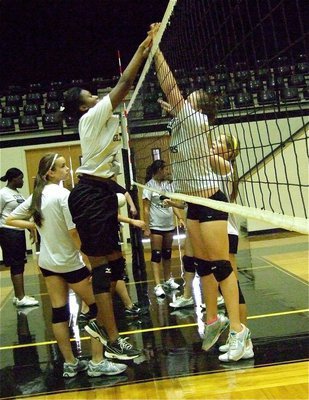 Image: JV Players Janay Robertson and Lilly Perry touch above the net as part of their exercises.