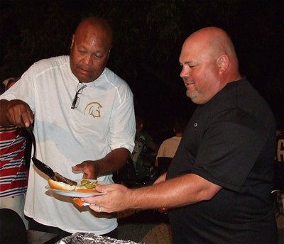 Image: Coach Mayberry loads Coach Wayne Rowe’s plate with a burger.