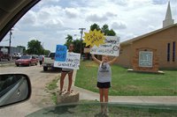 Image: Ashlyn Jacinto and Halee Turner invite drivers to a car wash fundraiser for Lady Gladiator Volleyball on Saturday in front of the First Baptist Church.