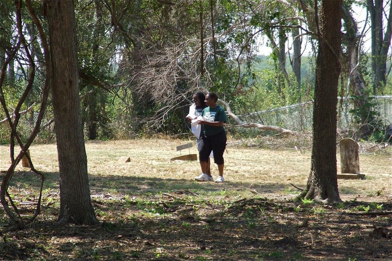 Image: Latricia Shaw and Dennis Perkins walk the WEST section of the St. Mary Cemetery property where their ancestors are buried. The broken and hanging tree limbs are the resulting aftermath of a bulldozer that removed undergrowth without concern for the burial plots that were in harms way.