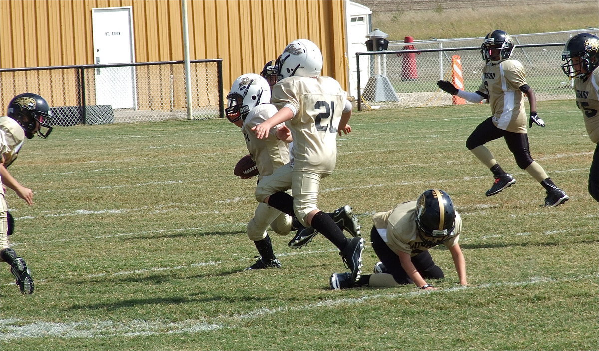 Image: Cade Brewer(21) tries to shield his A-Team Gladiator teammate, Ethan Itson(2), from Jaguar defenders as Itson maneuvers his way into the end zone.