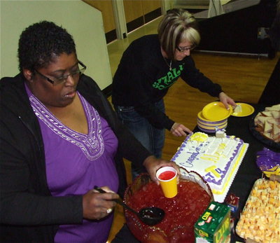 Image: IHS Faculty members Brenda Davis and Lisa jacinto serve cake, sandwich halves and cheese and crackers to guests after the signing.