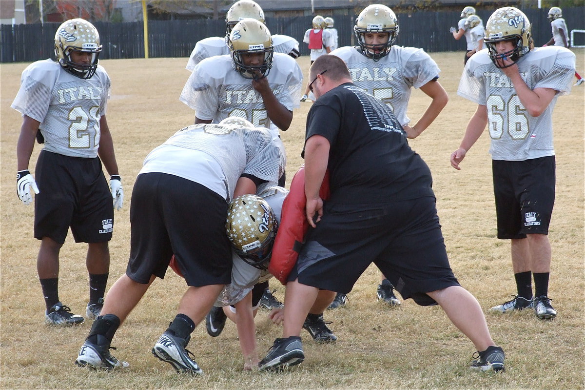 Image: Zain Byers(50) fights thru the gap against Kevin Roldan(60) and line coach Brandon Duncan as teammates Jalarnce Lewis(21), Justin Robbins(65), Cody Medrano(75) and Kyle Fortenberry(66) study up.