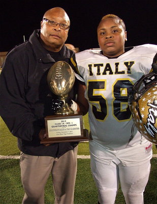 Image: Assistant coach Larry Mayberry, Sr. poses with his son Darol Mayberry(58), a junior lineman for Italy, and with the regional quarterfinal championship trophy.