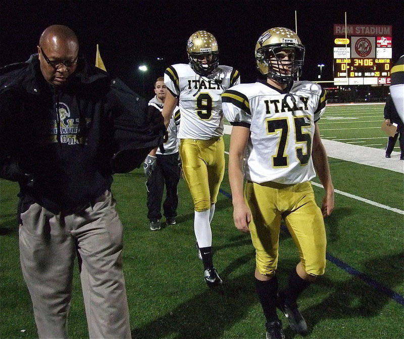 Image: Assistant coach Larry Mayberry, Sr. gears up as Cody Medrano(75), Cole Hopkins(9) and Caden Jacinto(6) make their way back to the locker room before taking on Stamford.