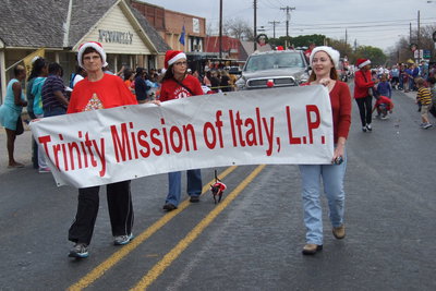 Image: Trinity Mission of Italy, L.P. holds up their banner while being escorted by a puppy on a leash.