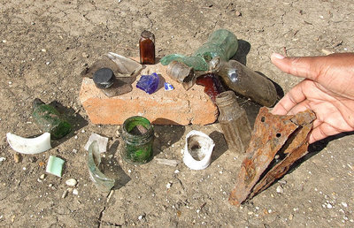 Image: Elmerine Bell displays a collection of damaged personal items that had been placed on head stones long ago but are now scattered across an empty field.