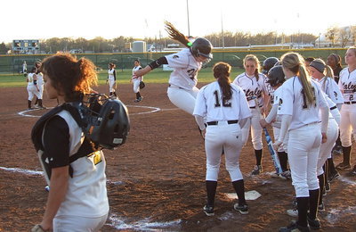 Image: And with a leaping statement, Alyssa Richards(9) stomps home plate after her game-tying homerun blast where she is cheerfully greeted by her teammates.