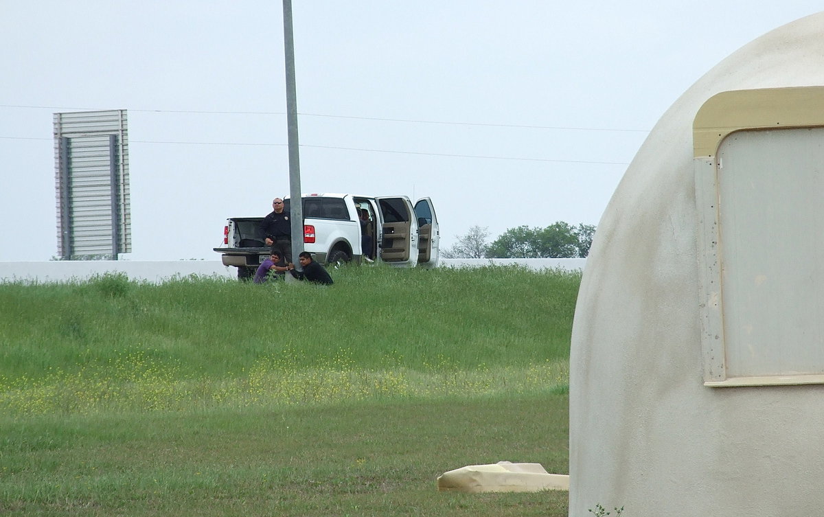 Image: Officers use a nearby light pole as a suspect rack as the men are cuffed while their partner in crime attempts to flee law enforcement after a traffic stop along Highway 35 in Italy near the Monolithic Dome Constructors, Inc. headquarters.