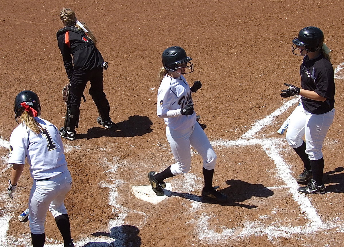 Image: Kelsey Nelson(4) reaches home plate and is greeted by teammate Jaclynn Lewis(15) while Bailey Eubank(1) clears the way.