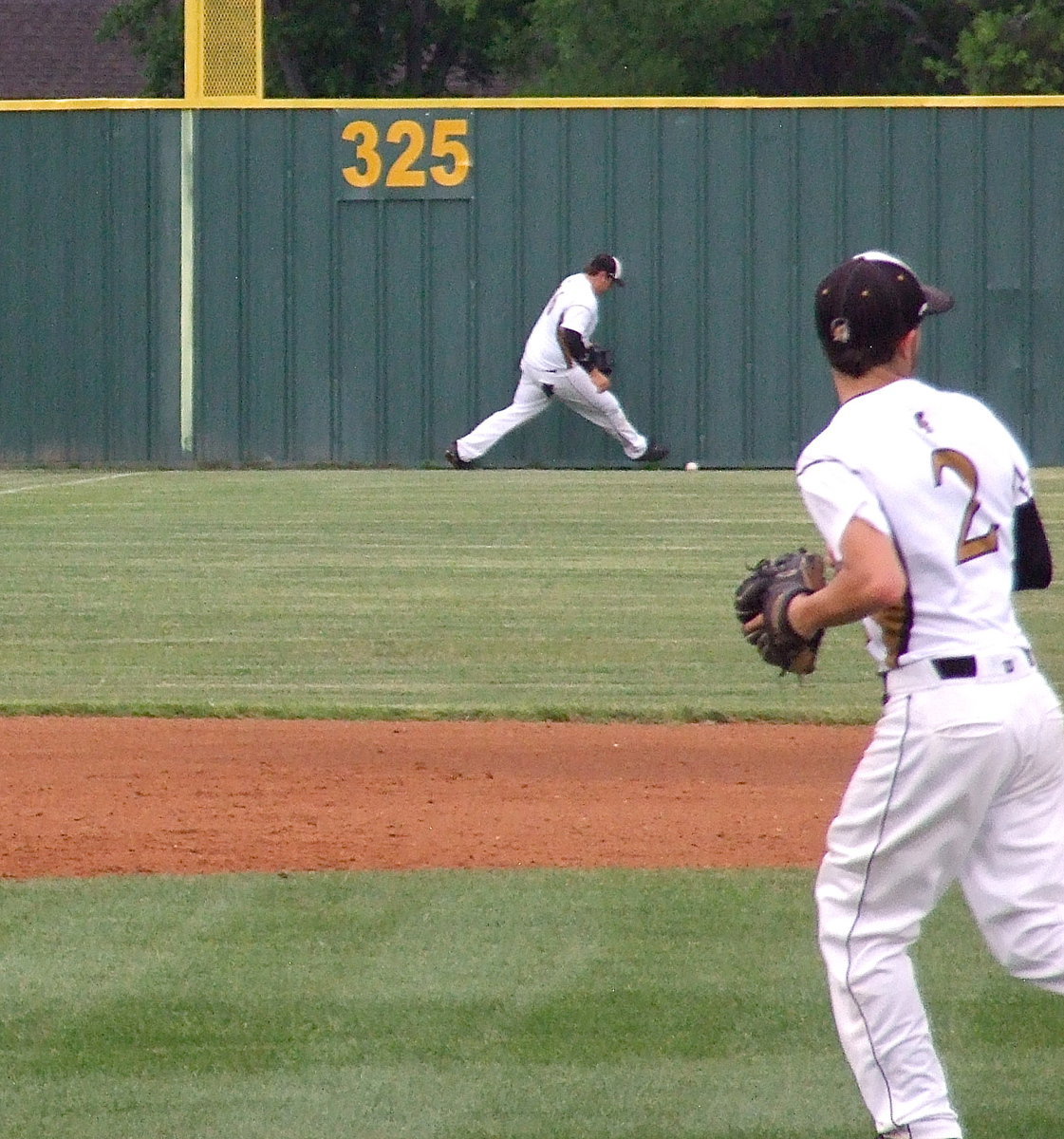 Image: Kevin Roldan(16) tracks down a ball at the base of the left field wall with teammate Caden Jacinto(2) getting into position to backup the relay throw from Roldan.