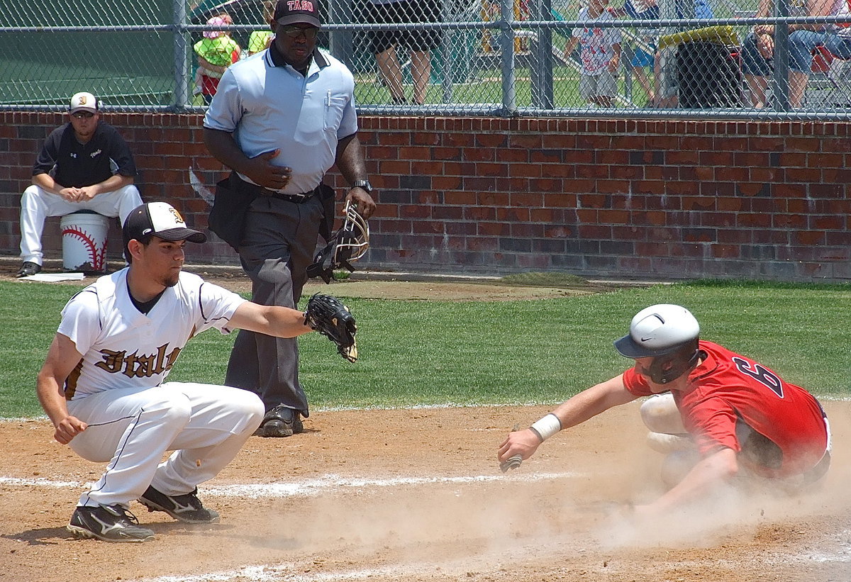 Image: Trenton slides home for a run with Italy’s pitcher Tyler Anderson(11) hoping to make the catch and a tag after a wild pitch gives the Trojans an opportunity.