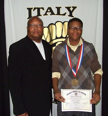 Image: Accompanied by Assistant Line Coach Larry Mayberry, Sr., senior Gladiator, John Hughes, displays his State semifinal medal and certificate of achievement.