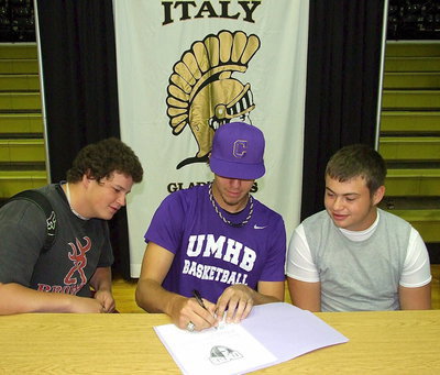 Image: The moment of truth: After the intensity of the signing party subsided and while guests were mingling, Cole Hopkins makes it official as he signs his letter of commitment to play basketball for the University of Mary Hardin-Baylor as close friends and teammates, John Byers and Zain Byers, seem in awe of the moment.