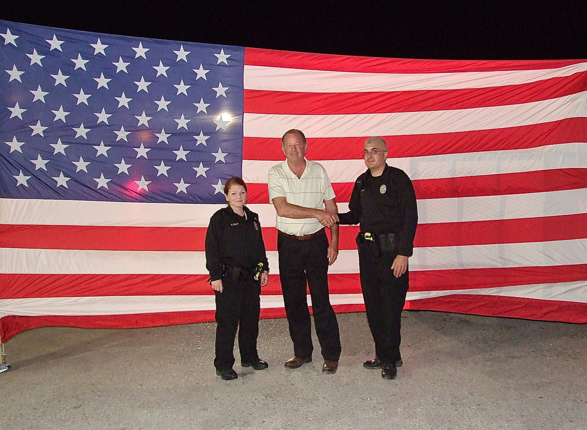 Image: City of Italy mayor, James Hobbs, is joined by Italy Police Department officers in front of an 18 foot long flag draped alongside Highway 77 to give Birdman a hero’s welcome into Italy.