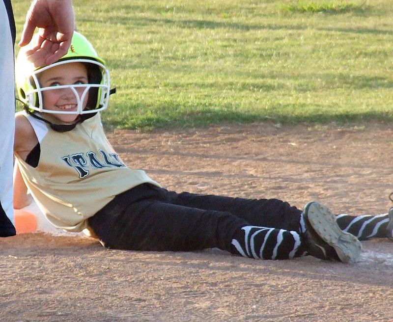 Image: Emily Janek reaches first but then slides down as she smiles up at her first base coach, Chris Ellis.