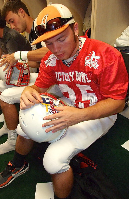 Image: Avalon Eagle Football’s and Red Team all-star, Reece Marshall, applies the FCA Logo decal to the sides of his helmet while in the locker room prior to kickoff.