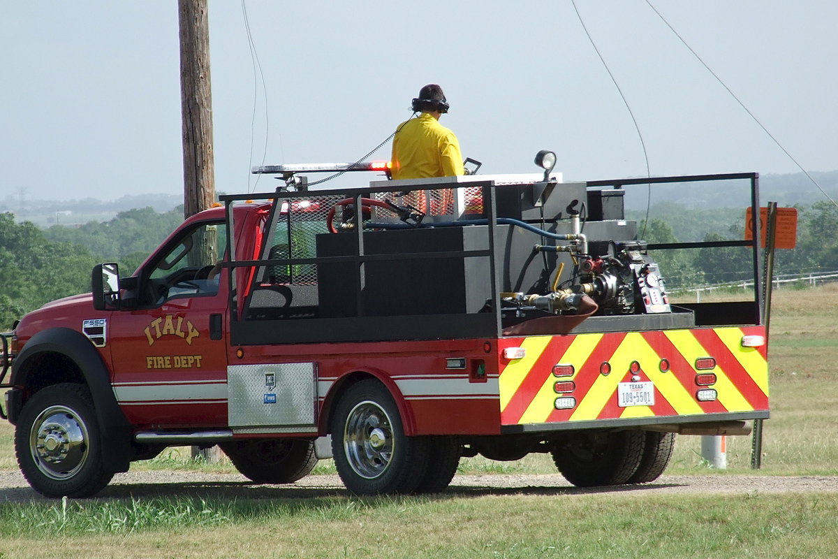 Image: After reaching the scene along Highway 77 and Martinez Road, Italy firefighters Brad Chambers, at the wheel, and Brandon Jacinto, manning the hose, communicate via headphones to avoid dangling power lines in an effort to saturate the resulting grass fire with water.