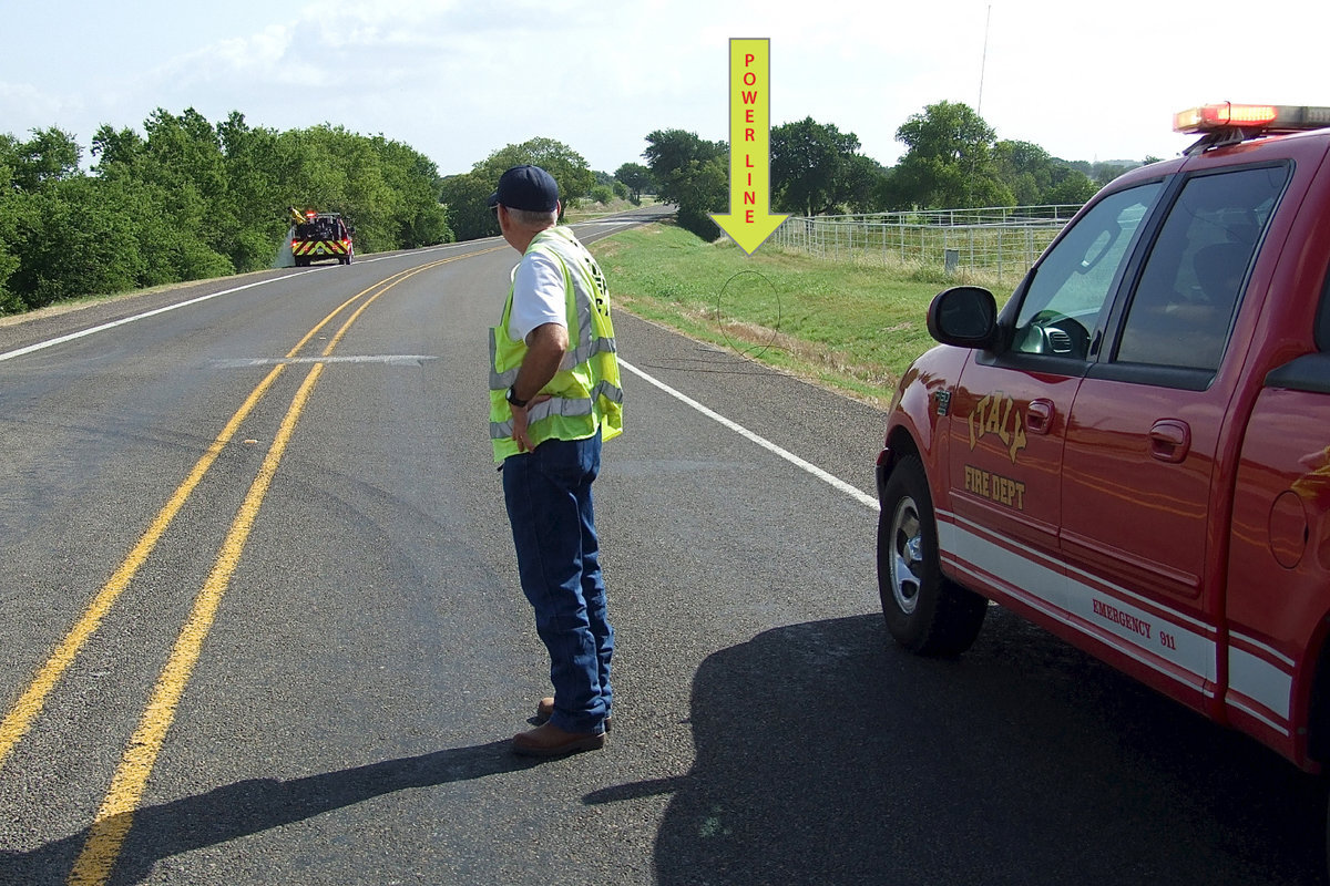 Image: Chief Chambers uses his rescue vehicle, as well as himself, to keep motorists from making contact with the downed power line while his fire crew works the fire on the opposite side of Highway 77.