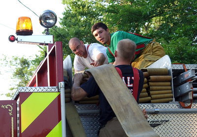 Image: Bryan Ward lifts the fire hose up to Brad Chambers and Brandon Jacinto who fold the hose back into place atop the fire truck.