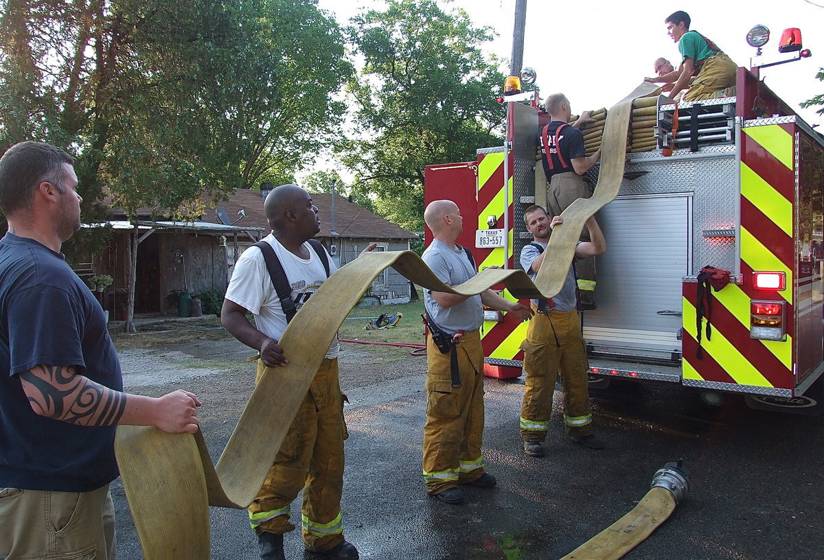 Image: Firefighters Justin Roberts, Lynn Lambert, Michael Chambers, Daniel Ballard, Bryan Ward, Brandon Jacinto and Brad Chambers work in unison to load the fire hose back onto the fire truck.