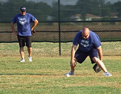 Image: Milford police Chief Carlos Phoenix takes a few pointers from teammate Brad Elliott who shows how not to field the ball.