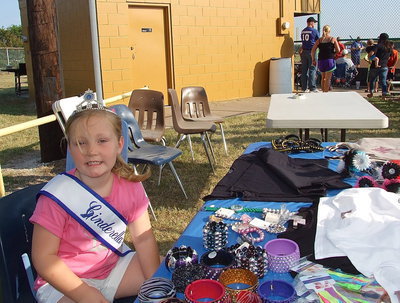 Image: 2013 Ellis County Cinderella Tot, Azlin Itson, helps sell women’s fashion accessories at a booth during the game.