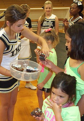 Image: With the camp at a close, varsity cheerleader Kristian Weeks passes out cupcakes to the campers as Hannah Carr and little sister Halee Carr take advantage.