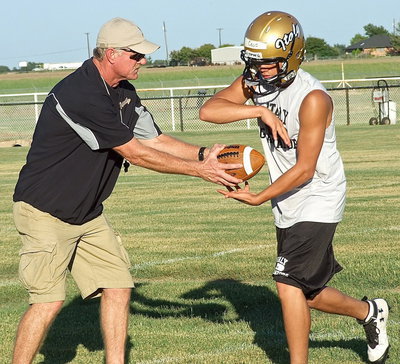 Image: Coach Tindol demonstrates handoff techniques to freshman Gladiator Joe Celis during the evening practice on Monday.