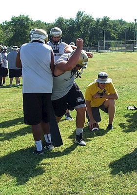 Image: With coach Jon Cady simulating the snap, senior Gladiator Kevin Roldan demonstrates the rip technique during a defensive line drill with teammate Darol Mayberry offering resistance.
