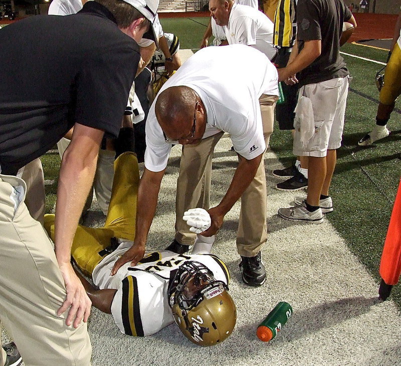 Image: Tre Robertson(3) returns a kickoff and then suffers leg cramps after the play as assistant coach Larry Mayberry, Sr., offers comfort.