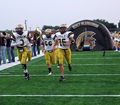 Image: Tre Robertson(3), John Byers(50) and Cody Medrano(75) charge out of the tunnel with the band and cheerleaders lining the route.