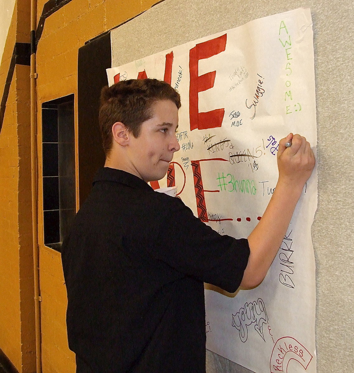 Image: Carl Jaynes, Jr., signs a banner by completing the phrase, “We Are…”