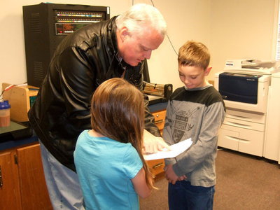 Image: Principal Nash helps Morgan Chambers and Jay Copeland (both 3rd graders) with what to say for the announcements.