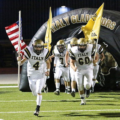 Image: With the band playing the fight song, Justin Wood(4), Kevin Roldan(60) and Ryan Connor(7) carry the flags as the Gladiators charge out of the tunnel for a memorable second-half.