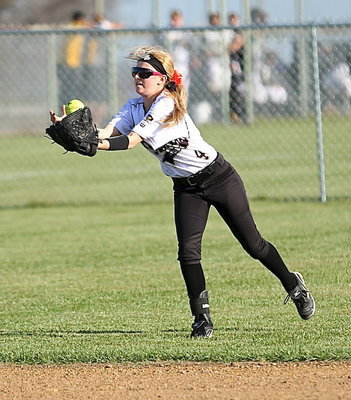 Image: Left fielder Britney Chambers(4) fights the strong winds to bobble into her mitt a fly ball for an out.
