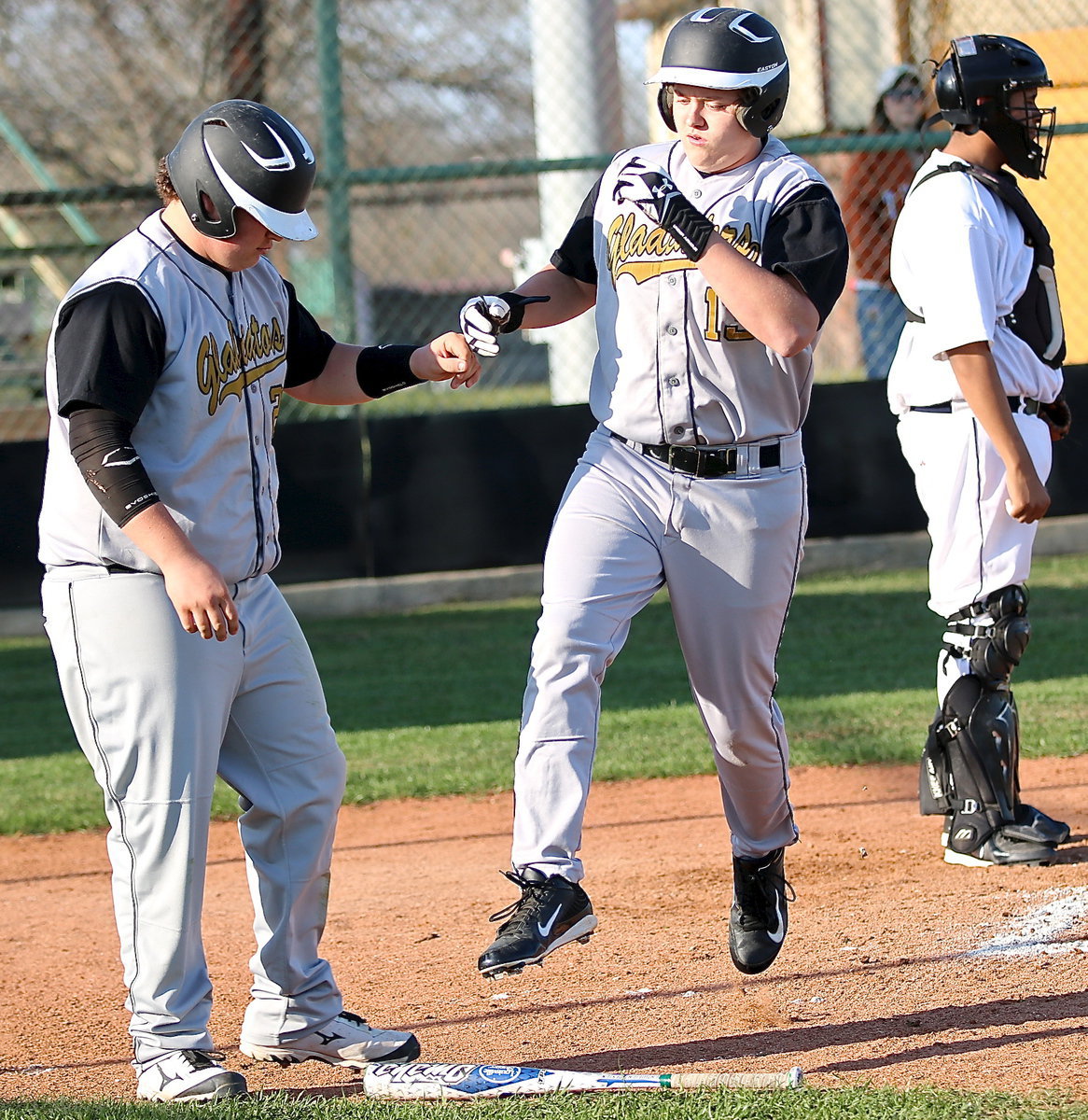 Image: Multitasking, Bailey Walton(13) scores a run, high-fives John Byers(18) and leaps over a bat.