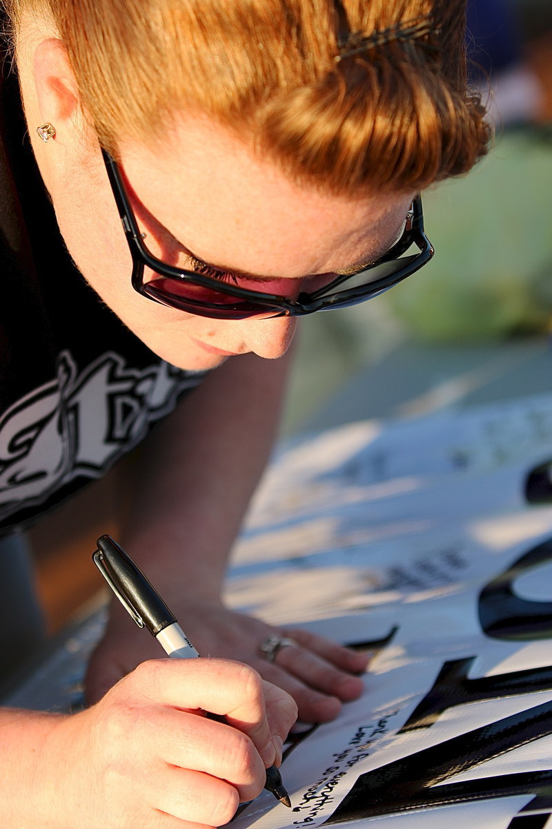 Image: Mistie Carter-Saxon writes a note on a banner to be presented to her former coach, Johnny Jones.