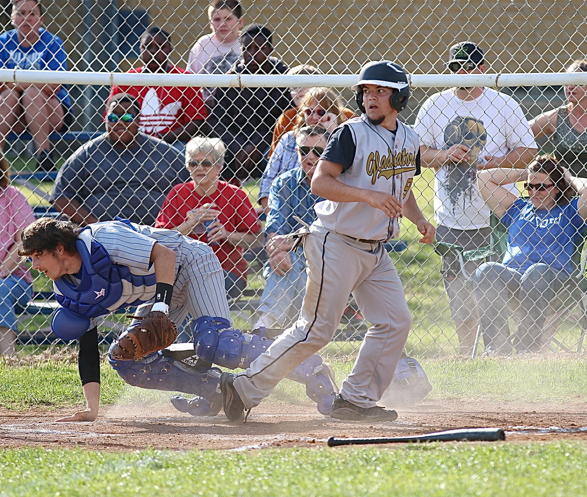 Image: Tyler Anderson(9) rises after sliding safely into home for another Gladiator run as the Bulldog’s Bryan Fedrick tries to regroup with runners still a running.