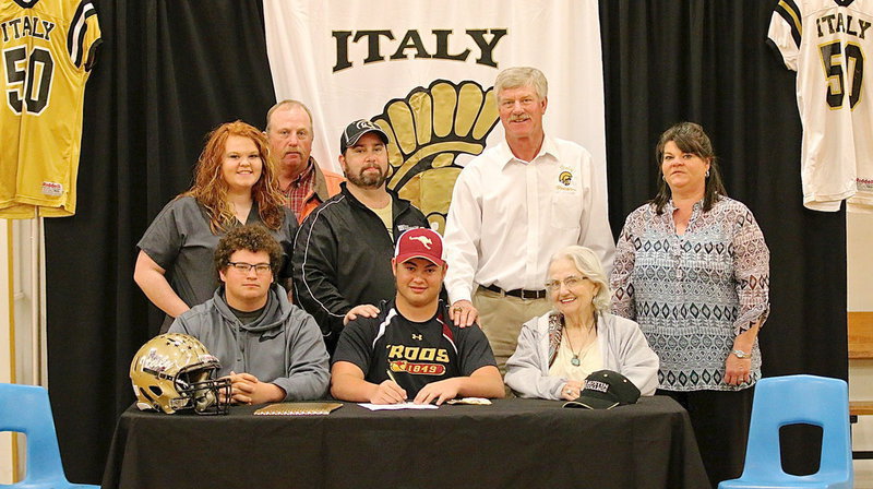 Image: Italy Gladiator Football’s Zain Byers, signs his commitment letter to play football for the Austin College Kangaroos in the fall of 2014. A signing party was held in Zain’s honor at the Italy High School campus on Wednesday. Back row (L-R): Katie Byers (cousin), Brentley Byers (uncle), Barry Byers (father), AD/HFC Charles Tindol and Nancy Byers (aunt). Front row (L-R): John Byers (cousin), Zain Byers and Ann Byers (grandmother).