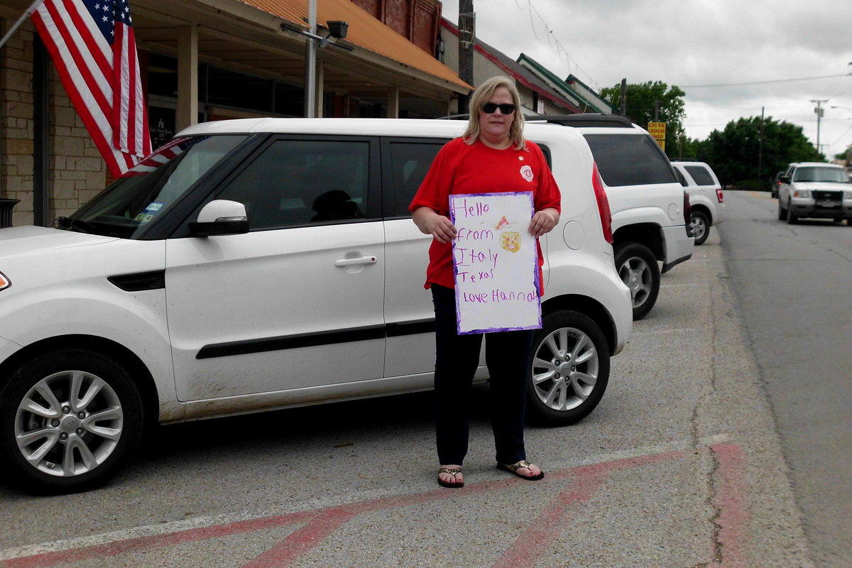 Image: Susan Harris holds a sign her daughter, Hannah, made to welcome the riders to Italy.