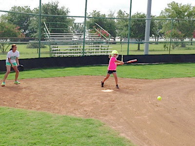 Image: Current Lady Gladiator star and camp coach April Lusk catches as future star Ella Hudson hits one toward first base.