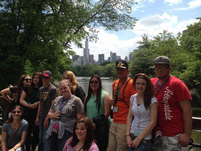 Image: With part of the New York skyline in the background, students stop on a bridge overlooking Central Park lake.
