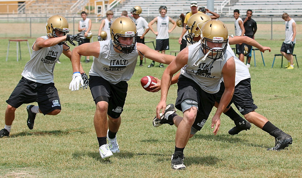 Image: Gladiators get rolling on their 2014 season as quarterback Joe Celis hands off to Levi McBride who follows Hunter Merimon and Coby Jeffords into the hole during 2-a-day workouts.