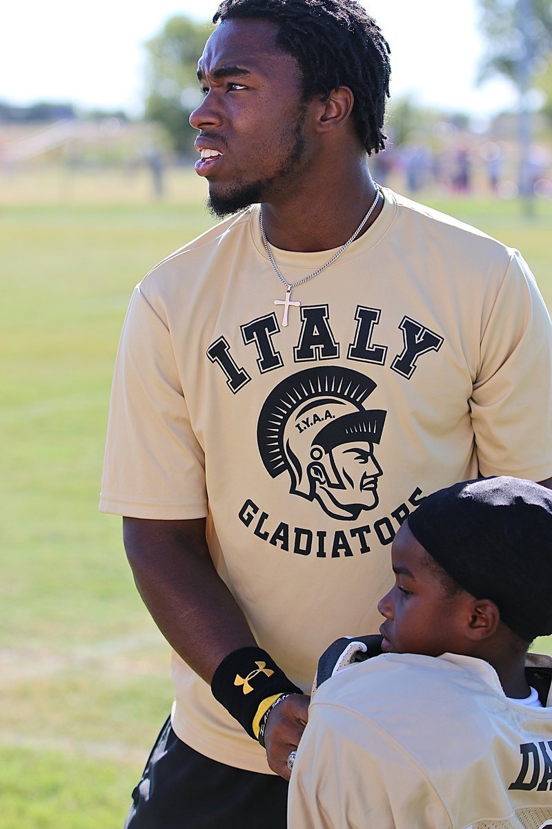 Image: IYAA C-team Gladiator head coach Jasenio Anderson helps Elijah Davis(18) buckle up for the battle against Mildred.