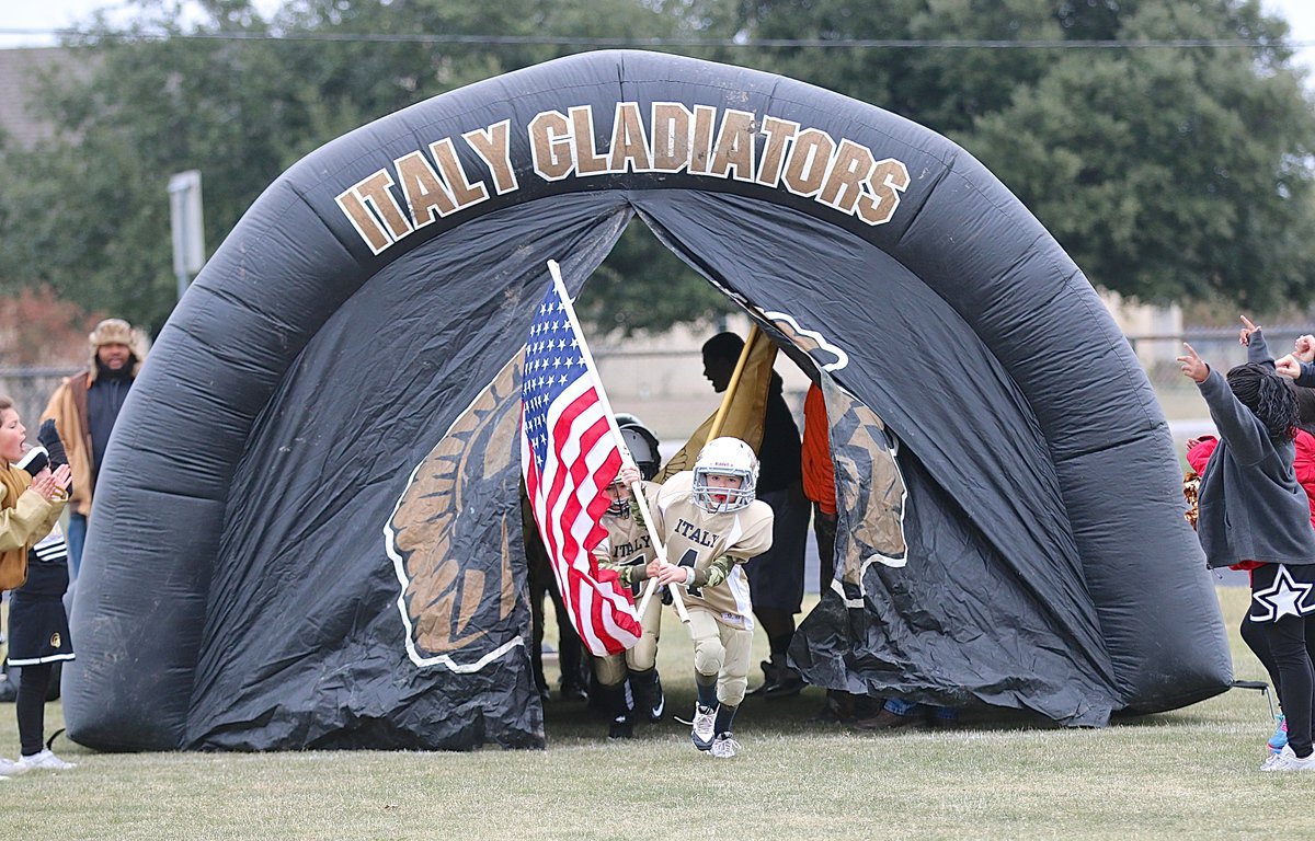 Image: The IYAA C-team Gladiators charge out of their tunnel to begin the 2014 NEH Superbowl with Gared Wood(4) and Damian Wooldridge(5) leading the way with flags held high.