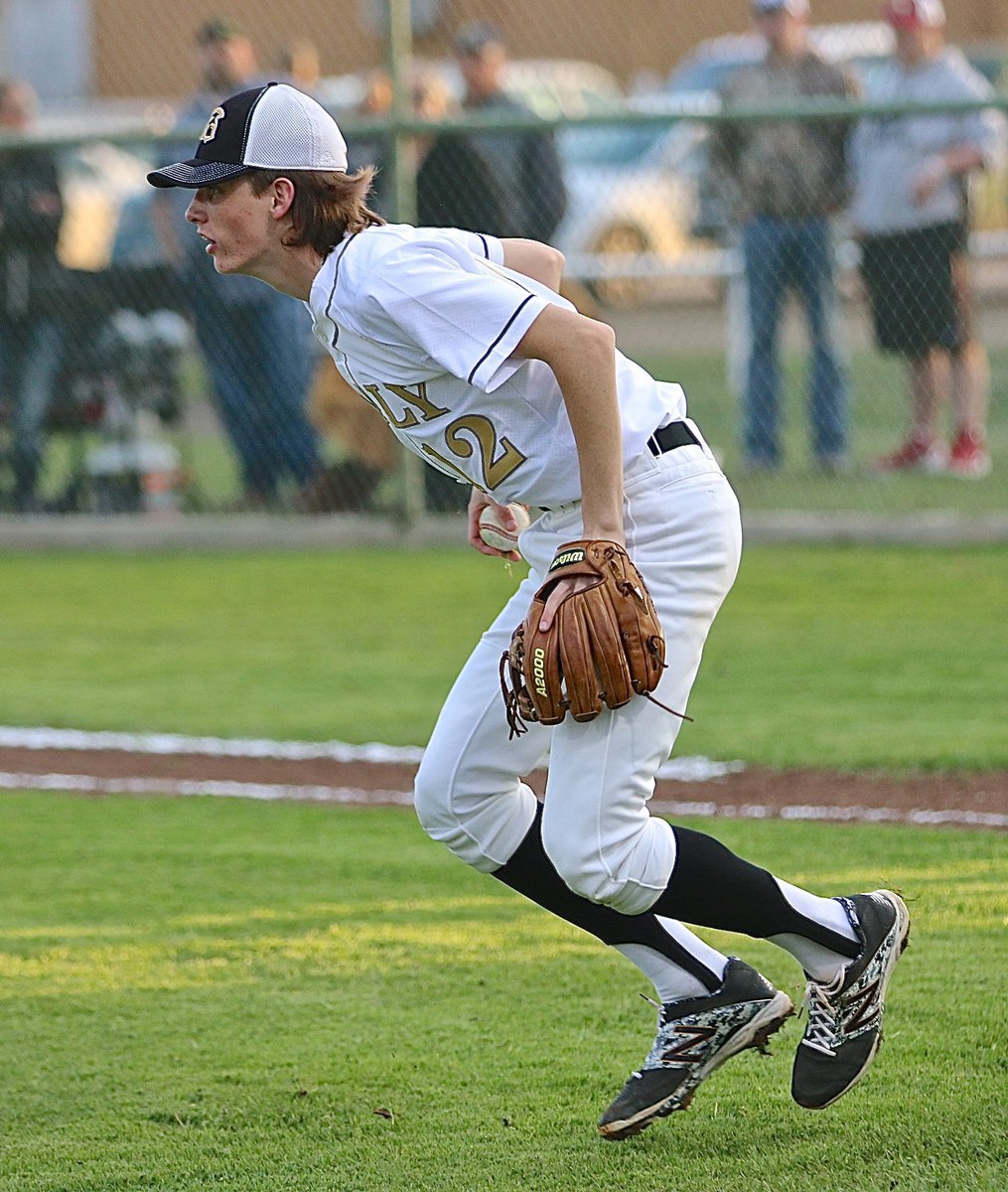 Image: Italy’s Ty Windham(12) scoops a short ball hit between his mound and home plate before turning and eagle-eyeing Eagle runners.