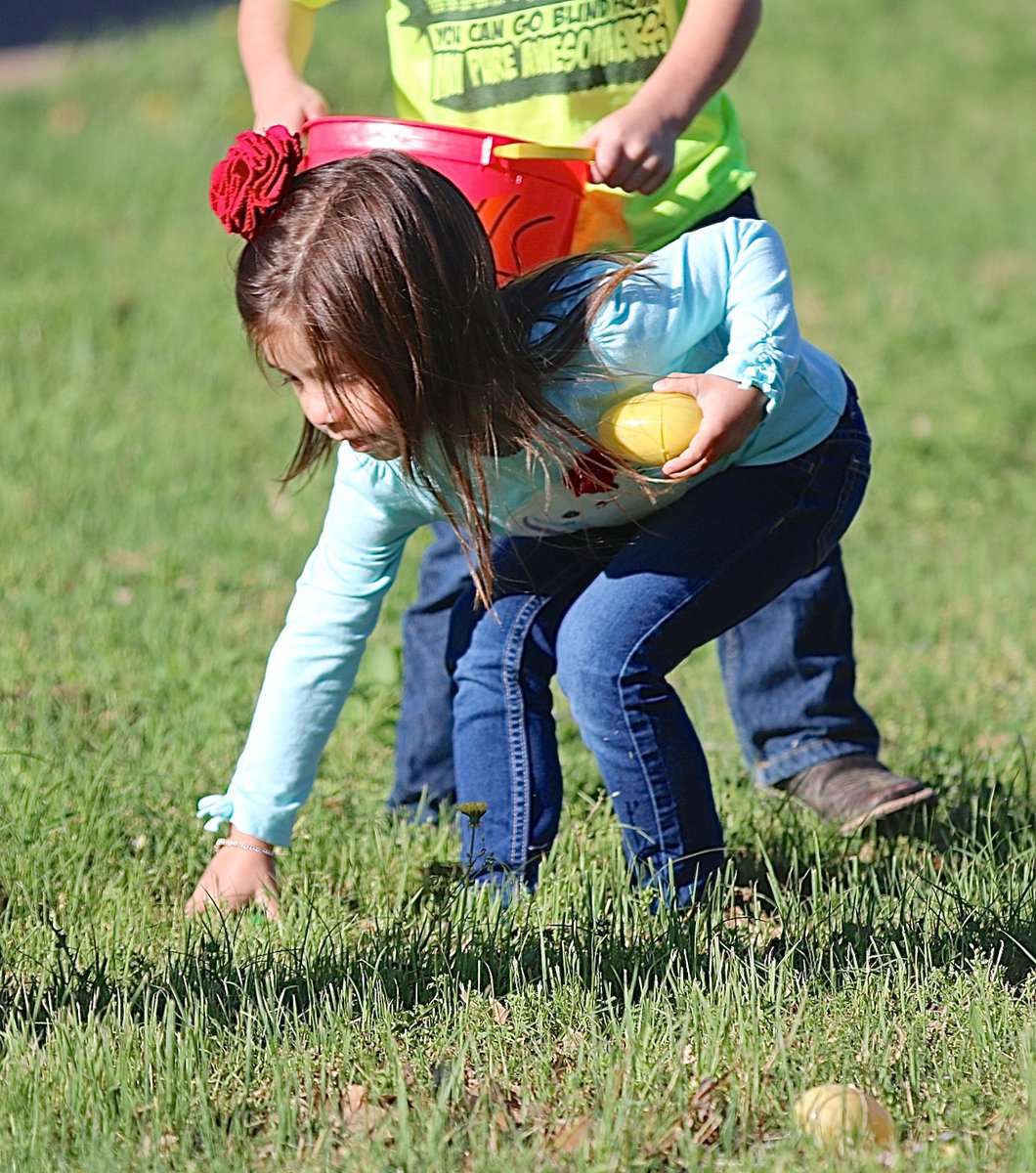 Image: With her bright red Easter bow highlighting the occasion, Avery picks up eggs one hand at a time.